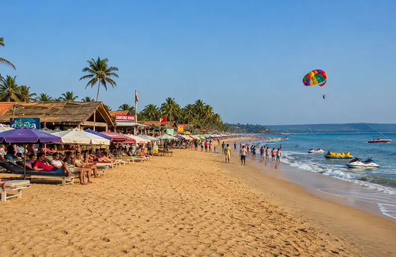 Candolim Beach with parasailing, beach shacks, and sunbeds.