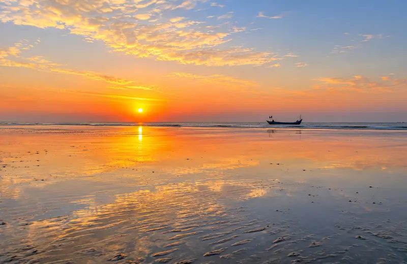 Sunrise reflection on the wet sand at Chandipur Beach Odisha during low tide, ideal for photography, with a distant fishing boat.