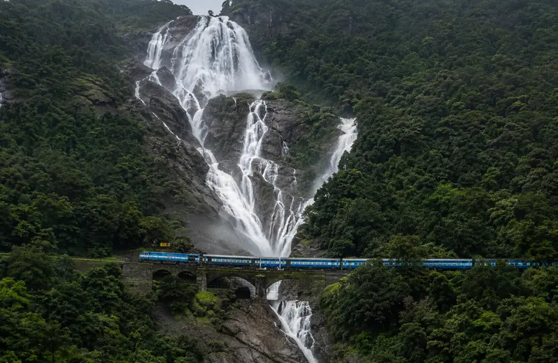 Dudhsagar Falls in Goa cascading in four tiers with a train crossing the railway bridge over the wat