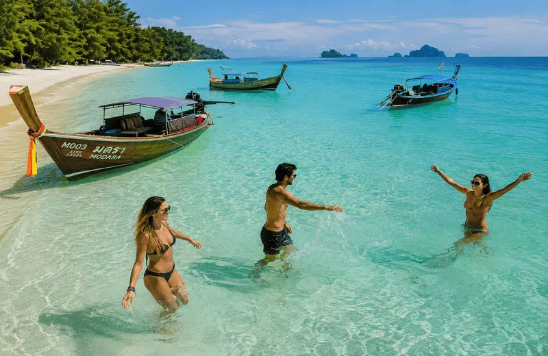 Tourists enjoying crystal-clear turquoise waters near longtail boats at Koh Kradan Beach, Thailand.