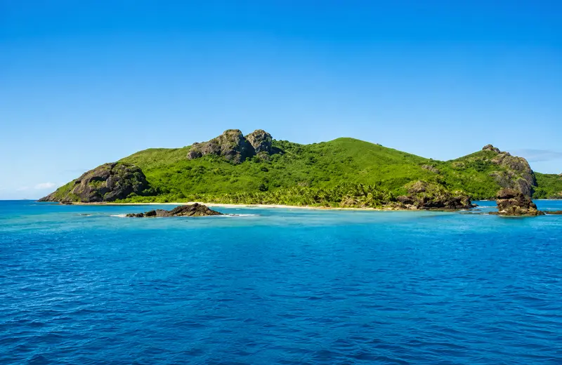 Lush green island with rocky peaks and turquoise waters in Fiji.